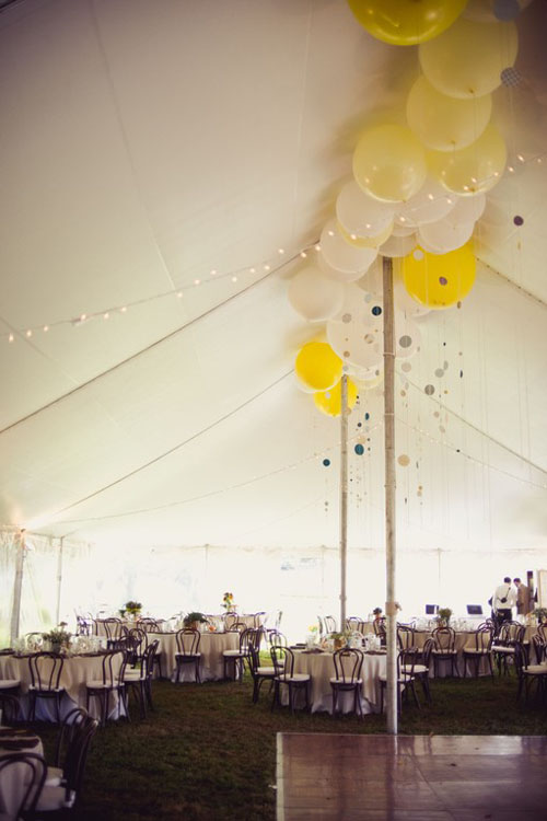 Yellow and white balloons in the top peak of a tent for a wedding reception