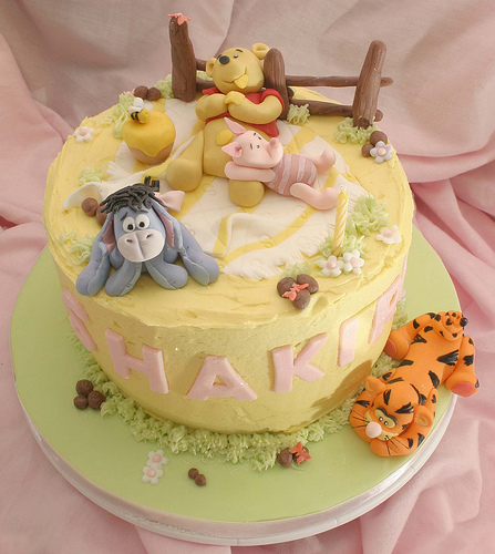 Winnie the Pooh, tigger, piglet and Eeyore resting on a birthday cake