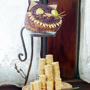 Cheshire cat cheese ball with almond teeth and apple eyes and tortilla ears and spaghetti whiskers over a stack of crackers