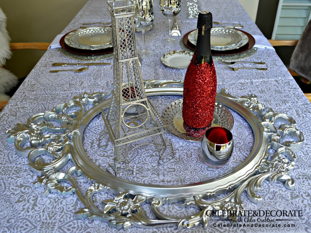 A-Paris-themed-Valentines-Dinner A silver and white tablecloth with a silver frame with a red glitter bottle of  champagne 