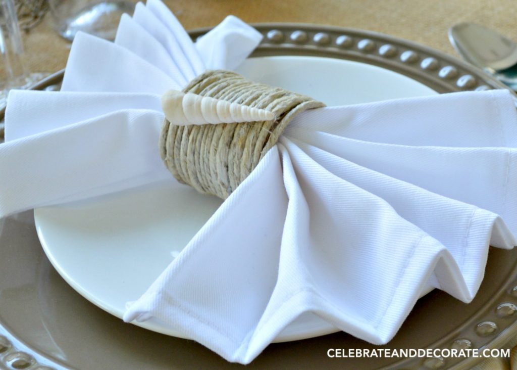  A close up of a seashell trimmed napkin ring on brown and white plates