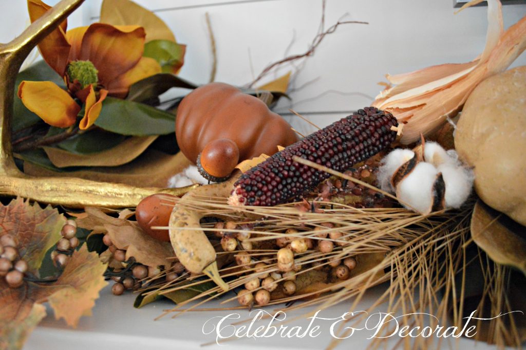 A lush Fall mantel in shades of gold and brown displays gourds, corn, acorns, antlers and cotton pods.