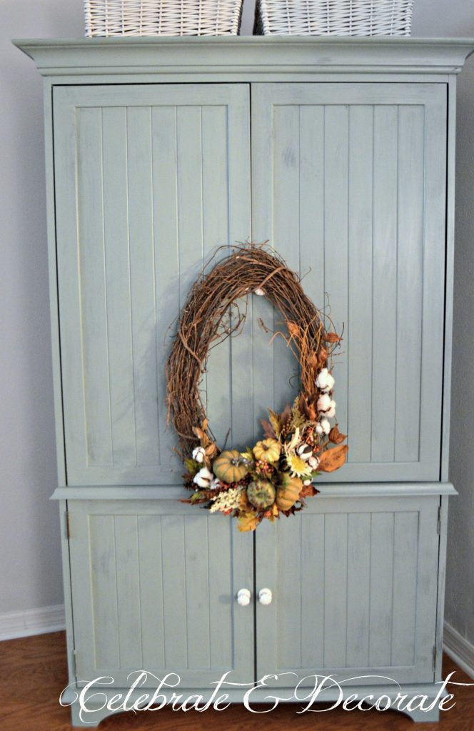 A pale blue milk paint armoire supports a pretty oval Fall wreath for a touch of Autumn decor in the bedroom.