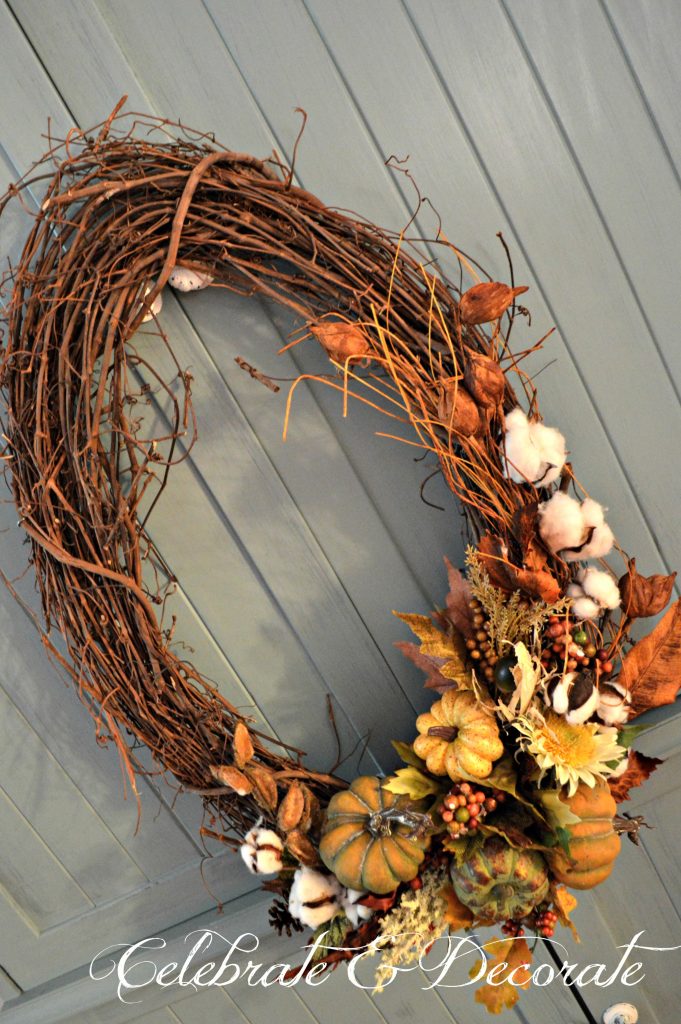 An oval grapevine wreath is decorated with cotton bolls, Fall leaves and pumpkins.