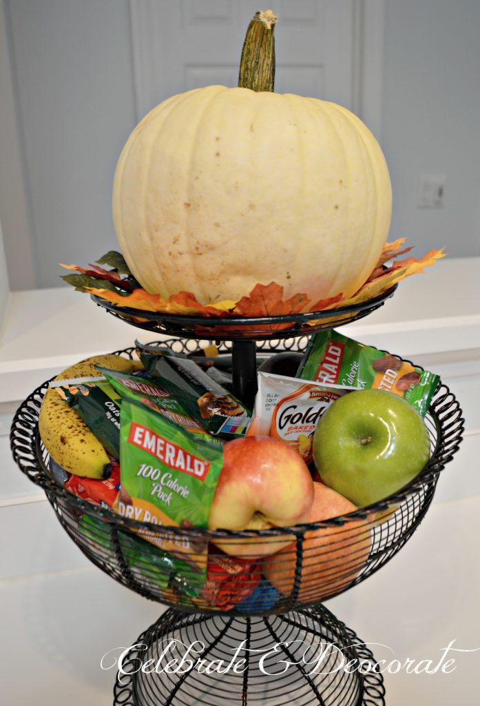 A White pumpkin adorns a tiered basket of snacks in the kitchen at this Fall Home Tour