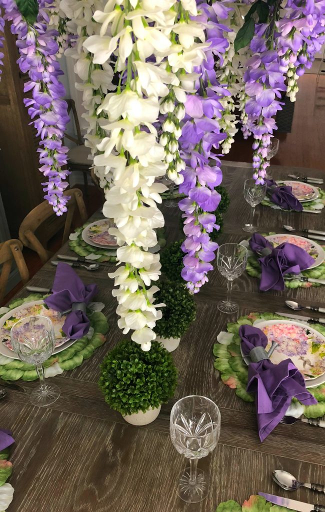 Wisteria hanging over a table set with floral plates and lavender napkins