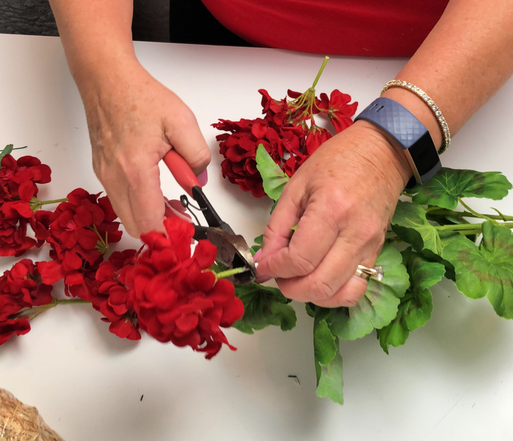 Using wire cutters to cut apart an artificial red geranium bush.