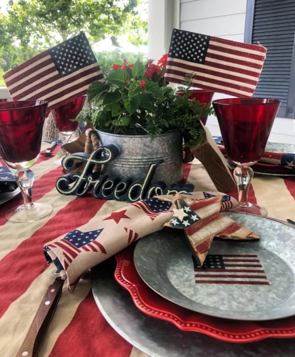A vintage style 4th of july tablescape with a galvanized bucket of red salvia for a centerpiece.  