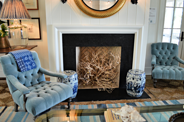 Coastal home fireplace with branches in the fireplace and blue chairs flanking the fireplace