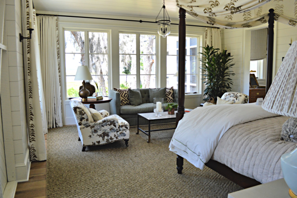 A master bedroom with neutral decor and accents of blue looks toward the inter coastal waterway through trees draped with Spanish moss.