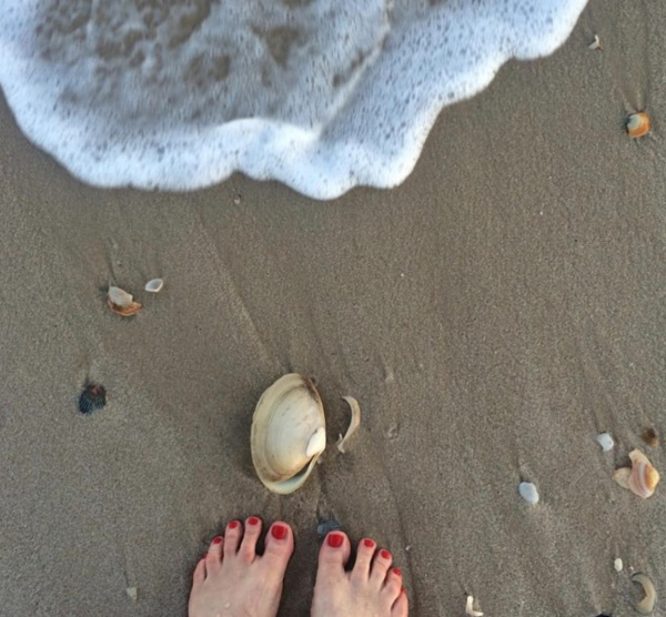 toes in the sand with the wave coming in and seashells on the sand