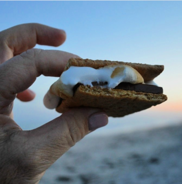fingers holding a s'mores with the sunset in the background