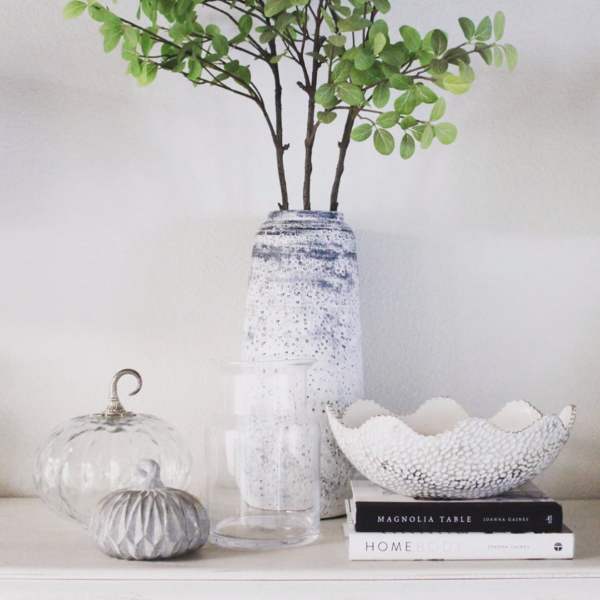a neutral or white fall vignette with glass crystal pumpkin, white vases and a gray wooden pumpkin and a white bowl on a magnolia table book