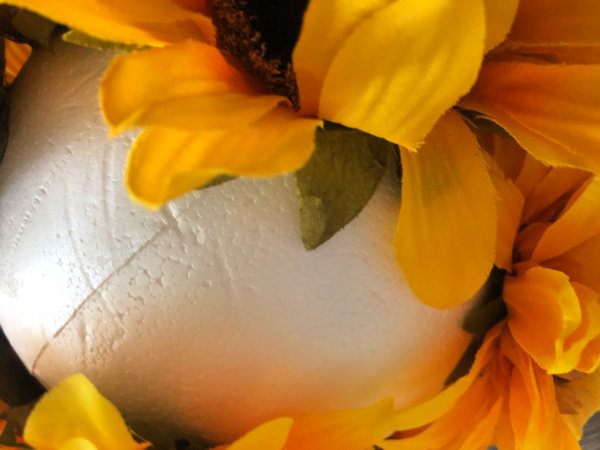 smooth styrofoam ball with faux sunflower blooms being glued to it.