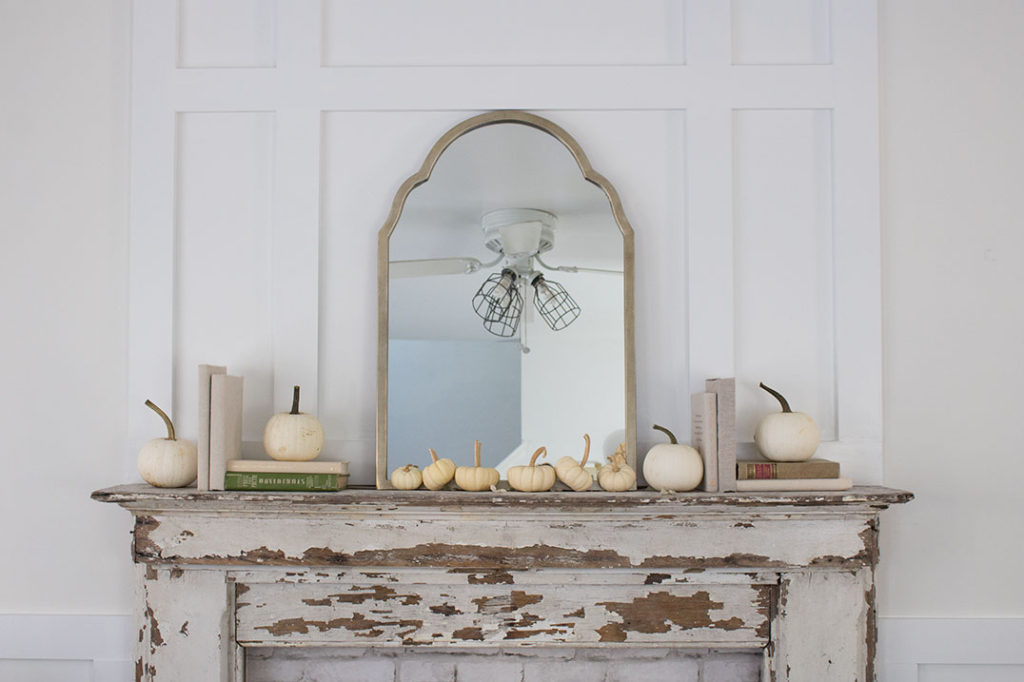 simple chippy mantel piece on a board and batten wall with a farmhouse simple arrangement of books and tiny white pumpkins with a mirror as the centerpiece