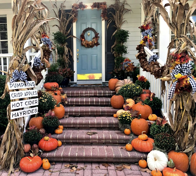 Front porch with brick steps decorated for fall with cornstalks, pumpkins and mums