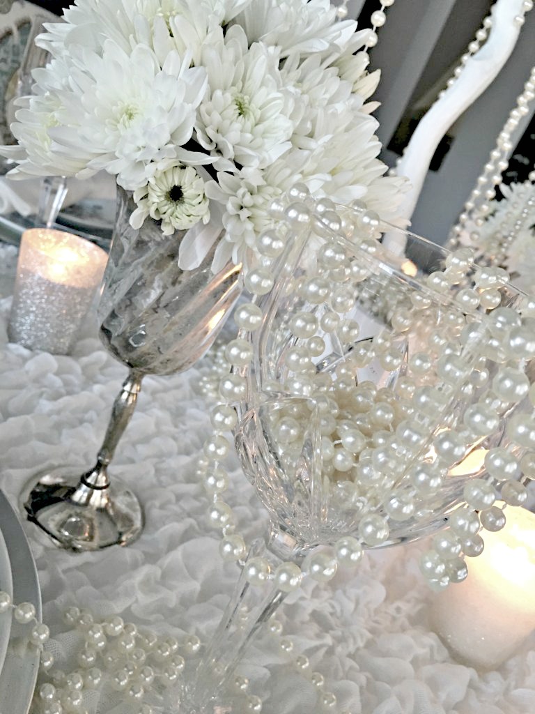 Stemware of silver and crystal with white flowers and white pearls set the scene for a winter tablescape