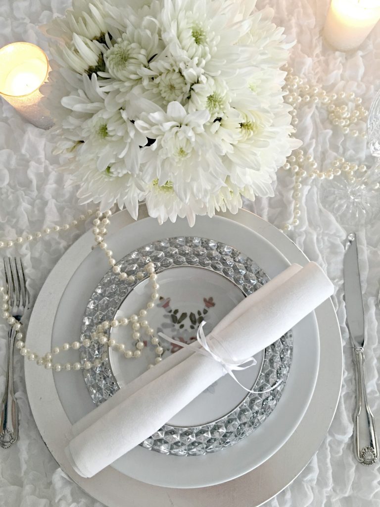 White and silver dishes with silver flatware and white mums adorn a winter white tablescape