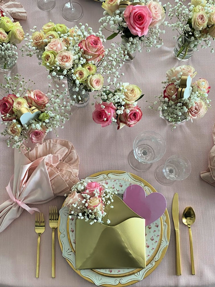 Vases of pink roses on a table along with a pretty valentine's place setting on a valentine tablescape