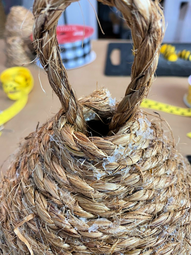 The top of a jute diy bee skep with a rope loop on the top and lots of hot glue on it that kind of looks like honey
