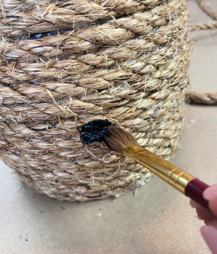 paintbrush painting a black spot on a jute decorative bee skep