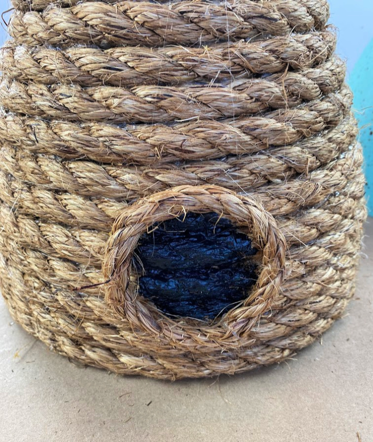 a decorative bee skep made with jute rope with a painted black circle on it for a "door" 