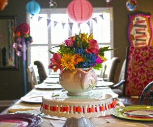 Alice in Wonderland Party table setting with colorful flowers in teapots, bright colored paper lanterns, and a colorful fabric bunting