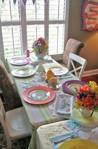 Alice in Wonderland table settings with colorful chargers and teapots filled with bright flowers