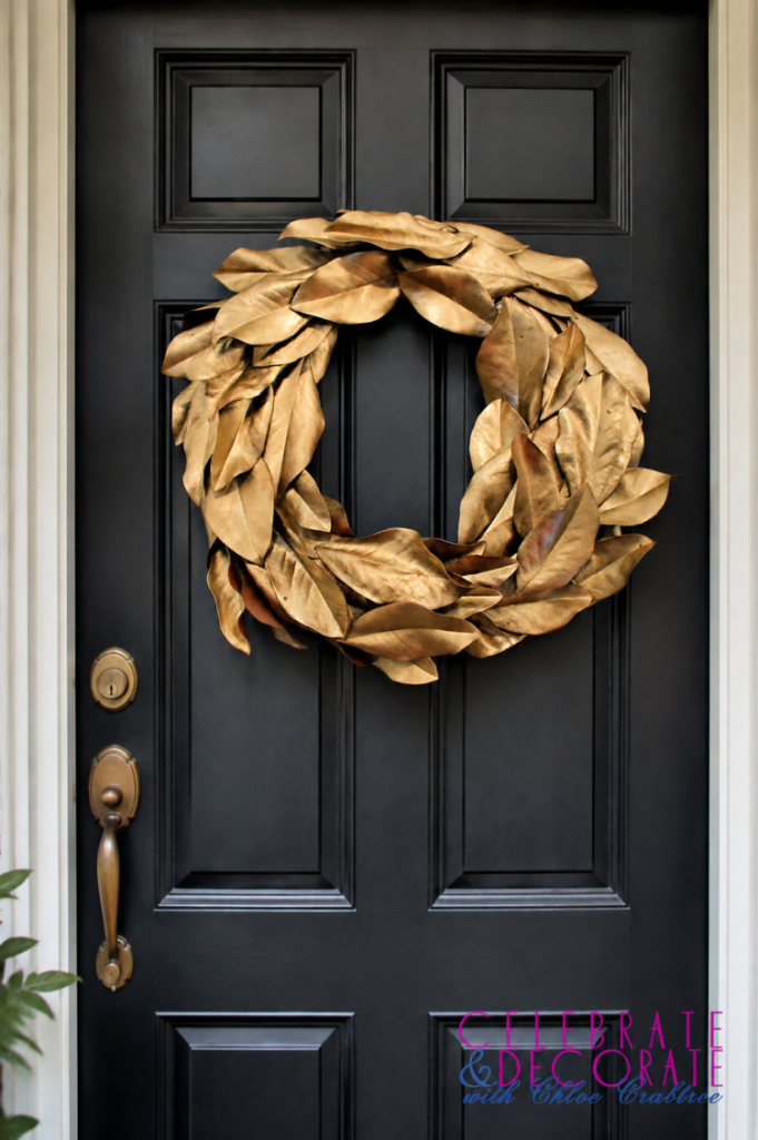 Gold magnolia leaf wreath displayed on a classic black paneled front door with aged brass hardware.