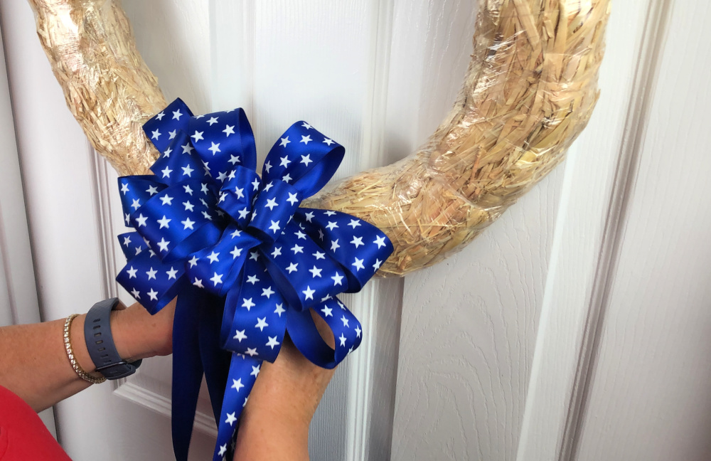 Attaching a patriotic bow to the bottom of a straw wreath