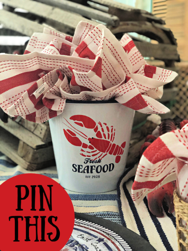 White tin pail with a lobster painted on it filled with red and white cloth napkins