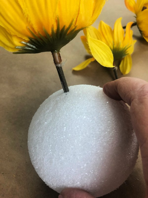 Faux sunflower stem being pushed into a styrofoam ball