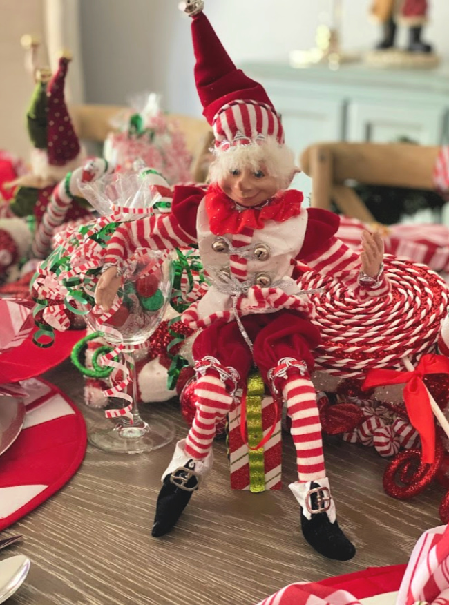 A peppermint themed elf sitting as a part of a christmas centerpiece