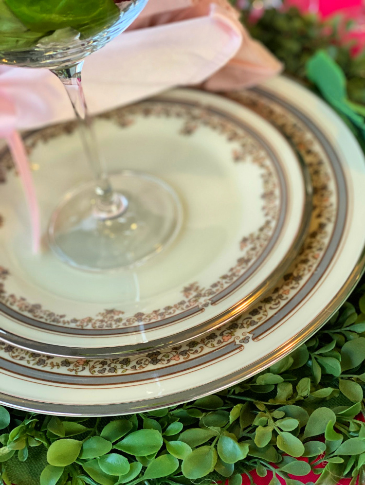 A close up shot of the edge of a china dinner plate topped with a matching salad plate.  Ivory china with a silver edge, gray stripe and soft pink and gray blooms 