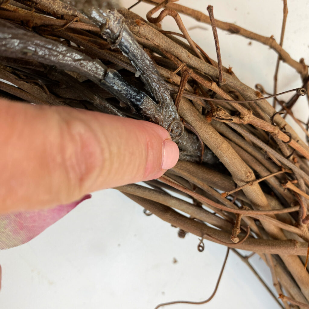 Hand showing how to weave faux stems into grapevine wreath