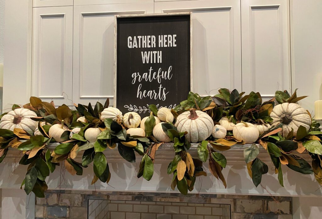 black and white sign on white mantel with magnolia garlands and white pumpkins