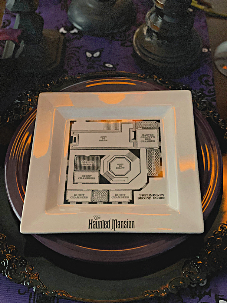 A black charger plate with a dark purple dinner plate and a haunted mansion salad plate on top.