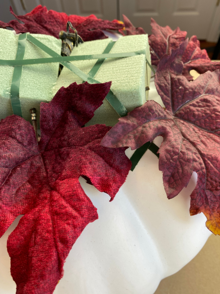  white pumpkin with dry floral foam on it and burgundy fall faux leaves stuck into the foam