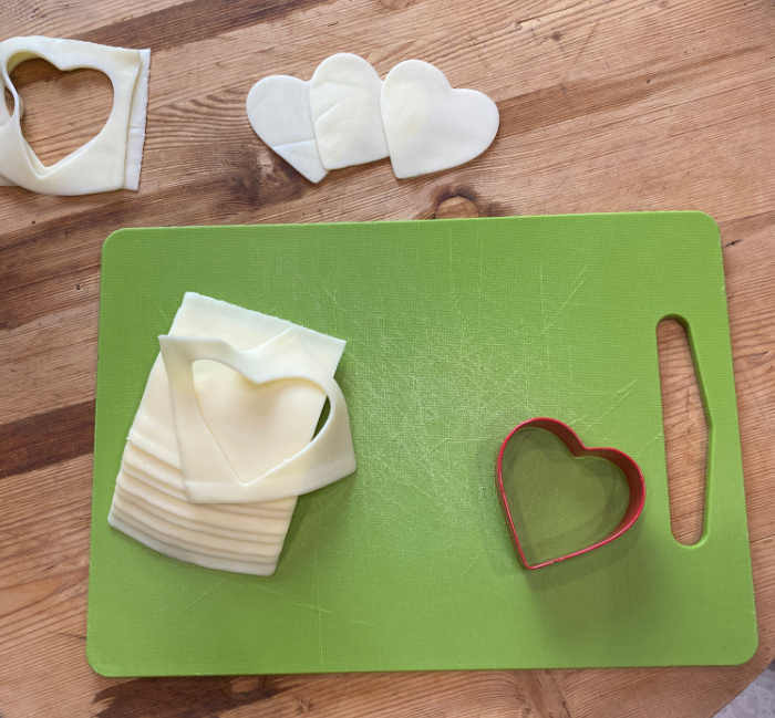 Green cutting board with cheese cut with a heart shaped cookie cutter.
