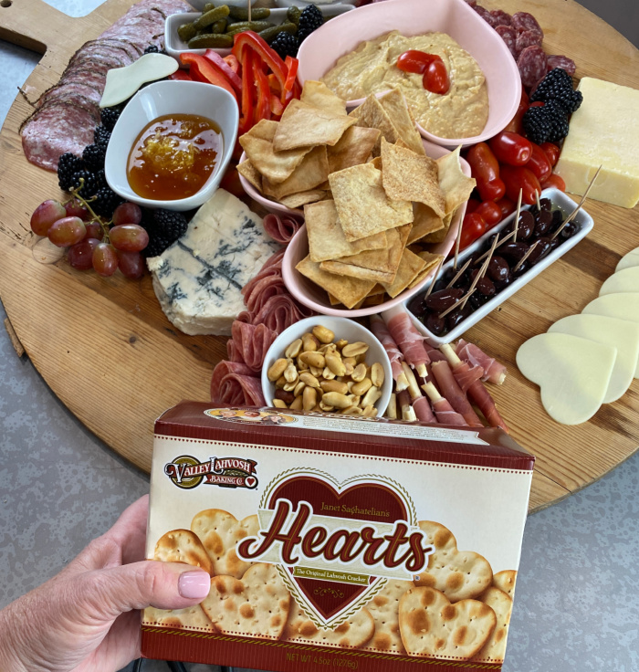 Wooden cutting board with heart shaped bowls of pita chips and hummus and cheese cut in heart shapes  Box of heart shaped crackers