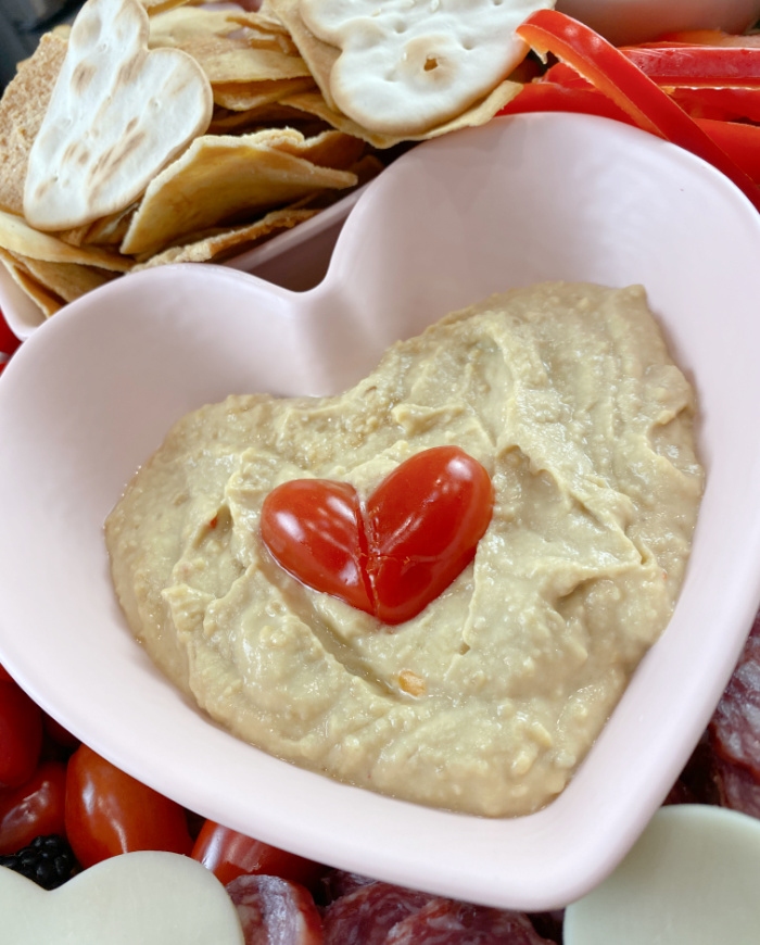 Heart shaped pink bowl with hummus and cherry tomatoes cut in a heart shape