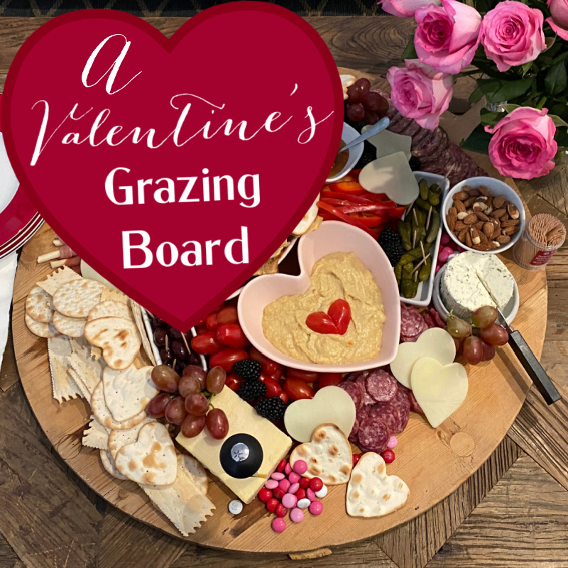 Valentine's grazing board with a heart shaped bowl of hummus and cheese and crackers in heart shaped.