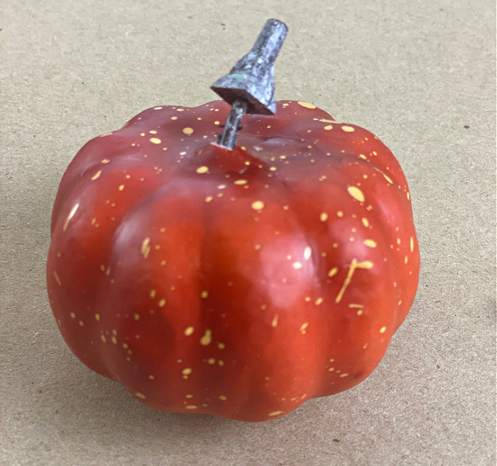one dark orange speckled faux mini craft pumpkin with the stem partially removed 