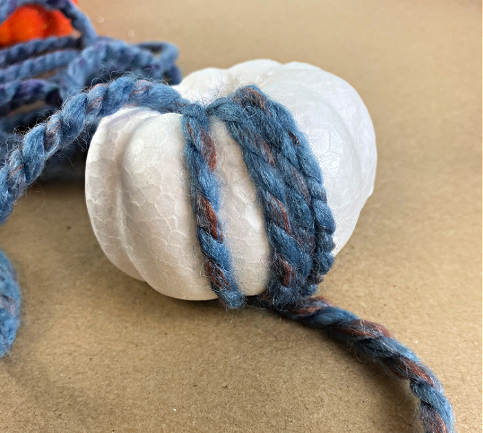 a white styrofoam pumpkin with a few strands of blue and rust yarn wrapped around it