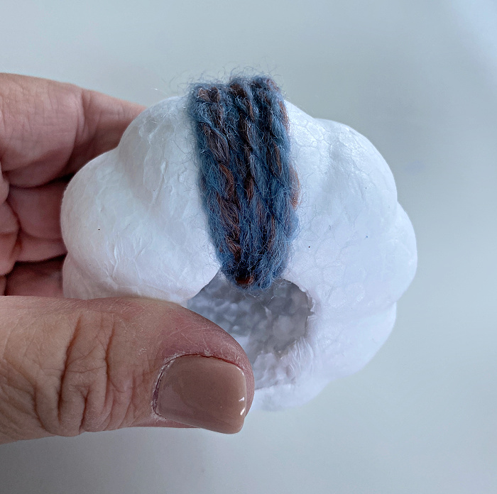 fingers holding a tiny styrofoam pumpkin wrapped with a few strands of blue and rust yarn
