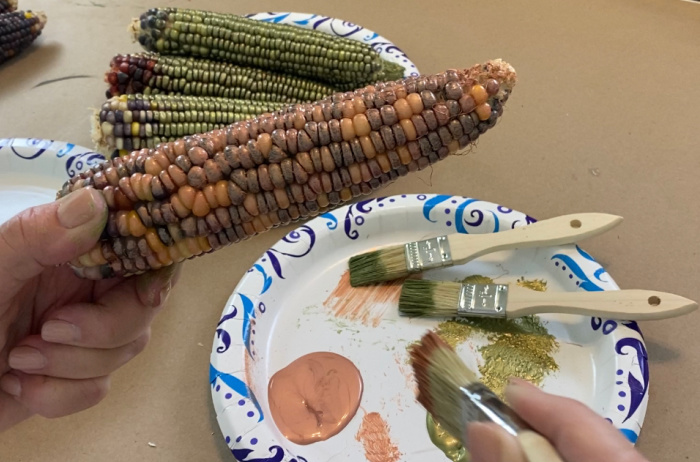 an ear of indian corn being painted with rose gold paint