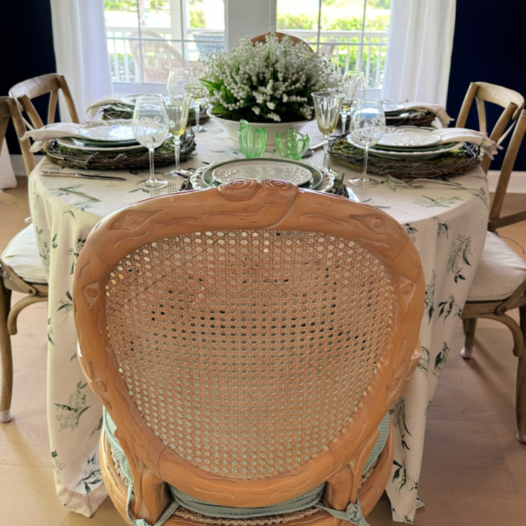 View of a tablescape looking at the back of a chair.  A lily of the valley theme, through the tablecloth, the plates and the napkins.  