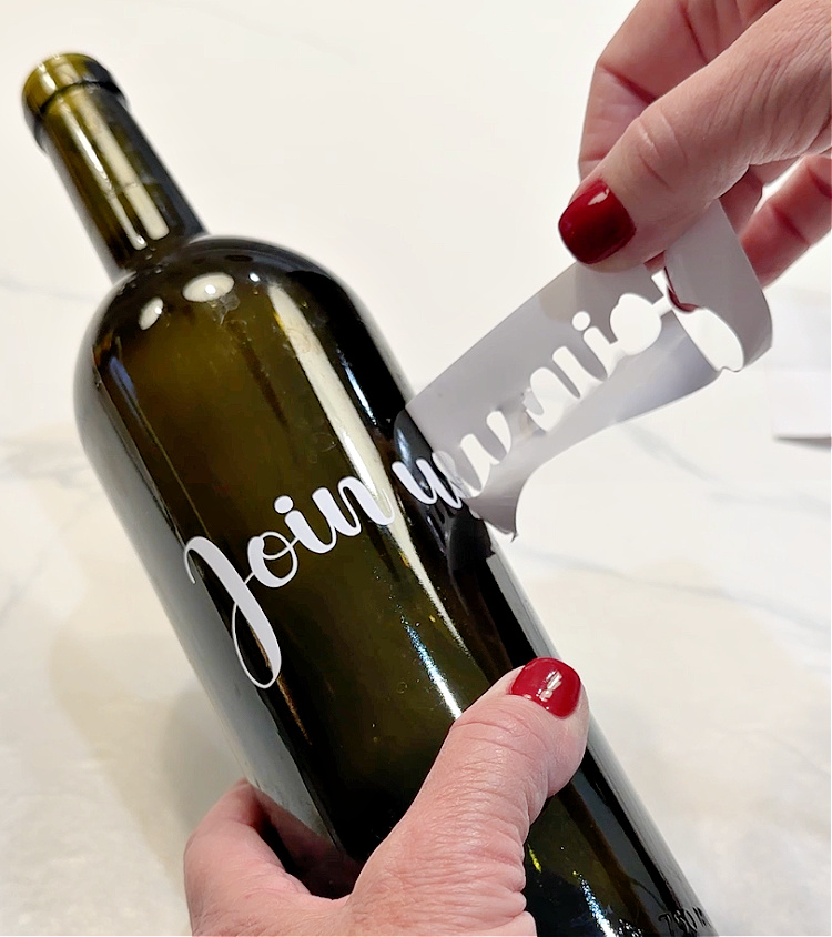 Hands peeling off the vinyl putting the words "join us" on the wine bottle.