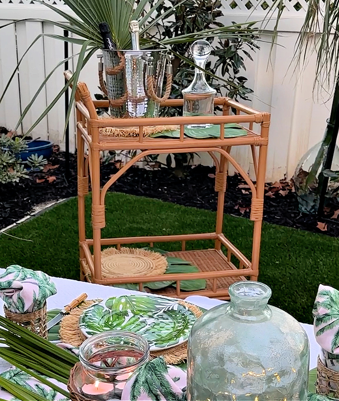 Tropical table setting with green and white tropical leaf patterned dinner plates on monstera leaf placemats and woven placemats.  Bamboo handled flatware.  