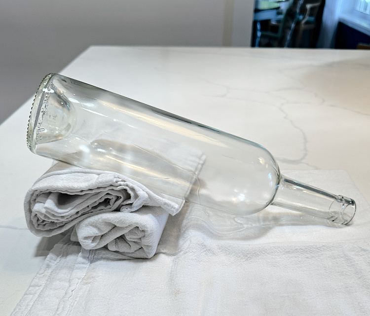 Empty clear wine bottle propped up on white kitchen dish towels.